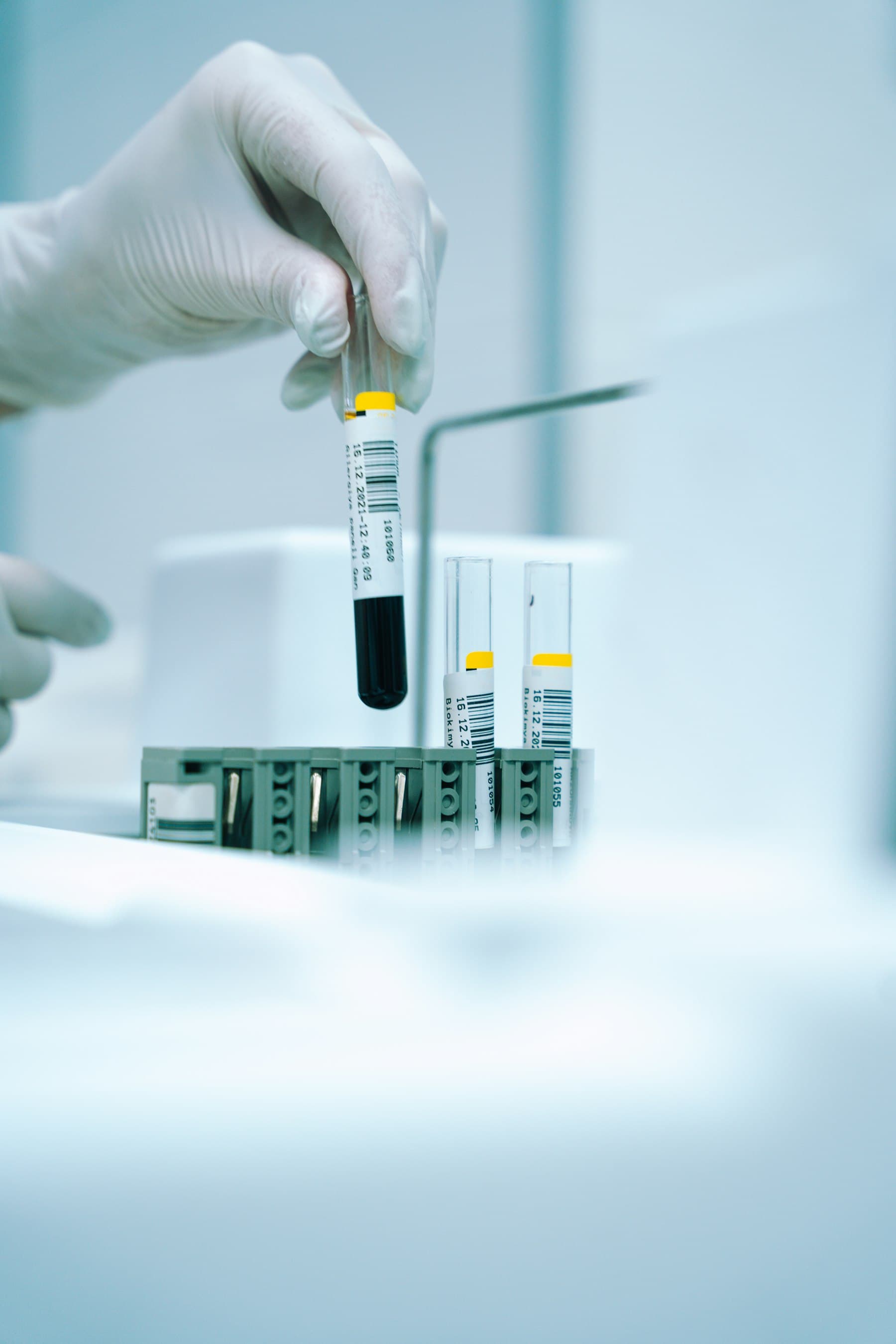 Gloved hand lifting a barcoded sample tube from a lab rack